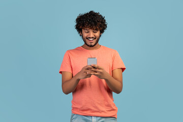 Wall Mural - Happy indian guy using mobile phone, blue studio background