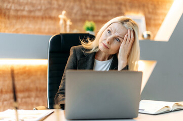 Wall Mural - Overworked exhausted sad caucasian mature blonde business woman, female top manager, office employee is tired from work, stressed, took a break from work, needs rest, upset looks to the side