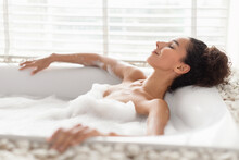 Side View Of Pretty Millennial Woman Relaxing In Foamy Bath, Lying In Hot Bubbly Water At Home, Copy Space