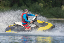 A Guy In Bright Clothes Rides A Jet Ski On The Lake. Entertainment On A High-speed Boat On The Water With Big Splashes. Summer Tourism And Recreation On The Water