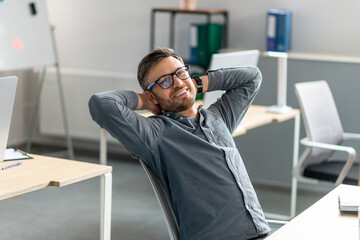 Poster - Confident middle aged company employee leaning on chair with hands behind head, relaxing and smiling at camera in office