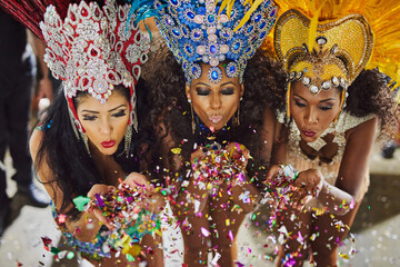 Spreading their magic through the night. Shot of samba dancers blowing confetti from their hands while performing in a carnival.