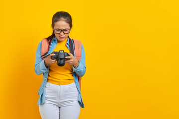 Wall Mural - Portrait of surprised young Asian woman looking at photo on camera isolated on yellow background. Passenger traveling on weekends. Air flight journey concept