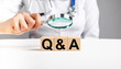 © valiantsin - FAQ in health and medicine. Doctor holding magnifier over wooden blocks with letters q a. Woman with stethoscope answers to patients questions about diseases treatment. High quality photo