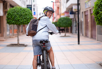 Sticker - Attractive smiling senior cyclist woman running with electric bicycle in a city street looking at camera. Elderly active grandmother enjoying a healthy lifestyle and free time in retirement