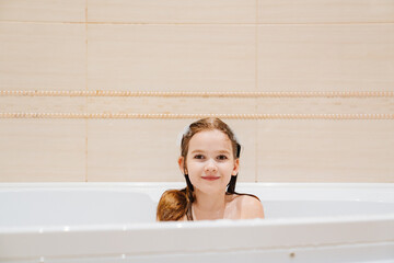 a little cheerful girl washes and plays in the bathroom.