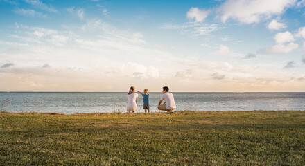 Wall Mural - Mother, father, and child relaxing together by the sea at sunset 