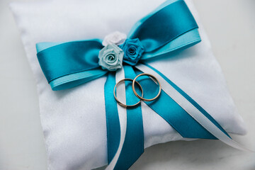 Two gold wedding rings lie on a festive pillow with a beryuz-colored bow, wedding details, wedding pillow, close-up