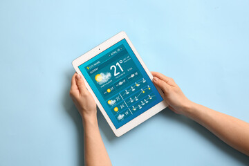 Young woman with tablet computer using weather forecast application on light blue background, top view