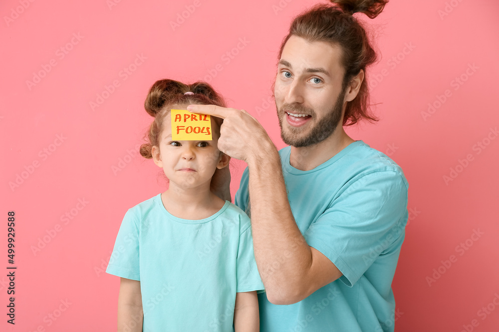 Father playing a prank on his little daughter against pink background. April Fools Day celebration