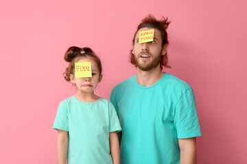 Poster - Funny man and her little daughter with sticky notes on their foreheads against pink background. April fools' day celebration