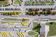 aerial view of bus depot with yellow buses and parking lot with parked cars. cityscape on sunny day.