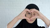 Fototapeta  - A beautiful woman in a black hijab shows a heart gesture which means love for everyone from the Muslim people. An Arab woman wearing a traditional Muslim headscarf smiles at the camera.