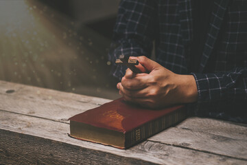 Wall Mural - Man holding wood cross on Bible on a wooden table. . Pray for god blessing to wishing have a better life. Believe in goodness. Power of hope or love and devotion.