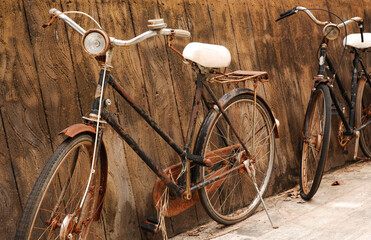 Two old vintage bicycles rusted near a concrete wall.