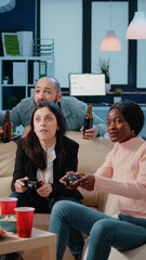 Wall Mural - Colleagues playing video games on console with controller after work. Cheerful coworkers enjoying fun activity on free time with drinks and snacks, using joystick on television to play