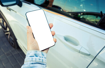 Woman holding mobile phone with blank screen next to door of her car in the street