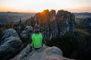 Wall Mural - Male hiker takes a break and enjoys mountain views. Sunlight on the rocky towers of Schrammsteine in national park Saxony Switzerland.