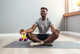 Fototapeta  - Man in sporty outfit doing yoga and meditating on an exercise mat. Sporty mindful man with tattoo meditating alone at home, peaceful calm hipster fit guy practicing yoga in lotus pose
