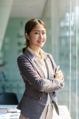 Beautiful young Asian business woman manager smiling looking at camera with crossed arms.