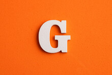 Alphabet Letter G - White Wood Piece On Orange Foamy Background