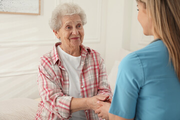 Canvas Print - Young caregiver talking to senior woman in room. Home health care service