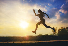 Silhouette Of Young Woman Running Sprinting On Road. Fit Runner Fitness Runner During Outdoor Workout With Sunset Background.