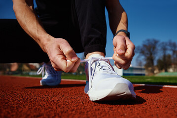 Male runner in white sneakers get ready for run at stadium track. Male hands tying on sport sneakers for jogging. Fitness and healthy lifestyle