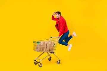 Poster - Full length body size view of attractive cheerful guy jumping carrying cart looking search goods isolated on bright yellow color background