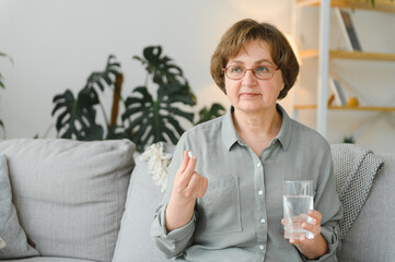 Sticker - age, medicine, healthcare and people concept - senior woman with glass of water taking pills at home