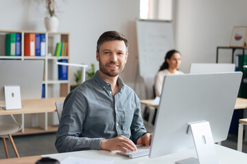 Poster - Handsome cheerful man sitting at desk, using modern computer in open space office