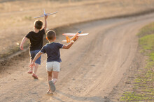 Two Little Boys Running On A Dirt Road Launching Toy Planes, Summer Outdoor Games
