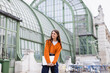 © LIGHTFIELD STUDIOS - pleased young woman in jeans and orange cardigan standing with laptop on rooftop of building.
