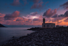 Breathtaking Scenic View Of A Lighthouse Surrounded By Pebbles On A Dramatic Sunset Sky Background