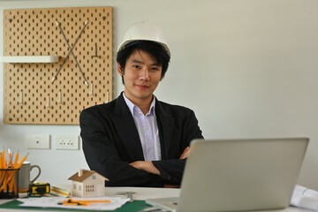 A portrait of an architecture wearing a helmet working on a tablet, laptop and tools in the office, for architect, business, safety and technology concept.