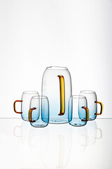 Poster - Vertical shot of a glass blue transparent  cups and juice pot with a white background