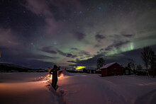 Northern Lights In The Arctic Winter With Snow And Chalets