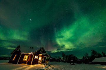 Northern Lights in the arctic winter with snow and chalets