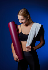 Sports girl, with a towel on her shoulder and a bottle of water in her hands, is resting after training in the gym