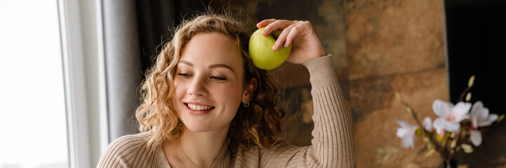 Wall Mural - Young white woman smiling and eating apple while working with laptop