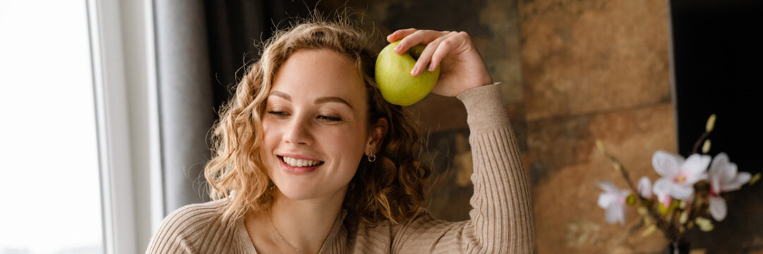 young white woman smiling and eating apple while working with laptop