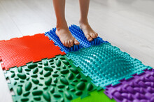 The Child Walks On An Orthopedic Massage Mat For Feet. Massage Mats With Different Stiffness And Texture.