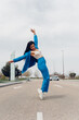 © Dani D.G - Young adult woman dancing break dance in the street. African teenager in stylish trendy blue outfit Dancing urban dance outdoors.