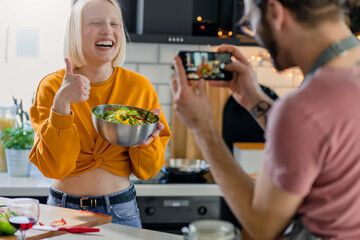 Young cheerful couple using smartphone while preparing a healthy vegan lunch at home