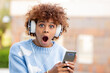 african american girl with headphones surprised looking at mobile phone