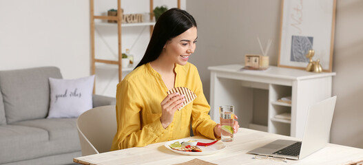 Sticker - Beautiful young woman with laptop eating tasty Mexican quesadilla at home