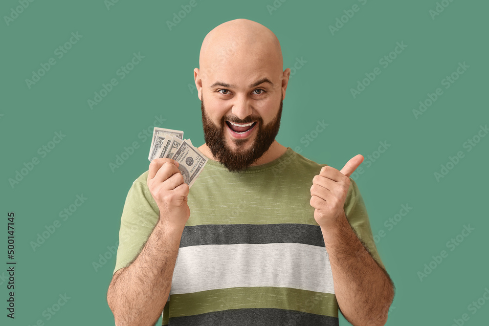 Happy bald man with money showing thumb-up on green background