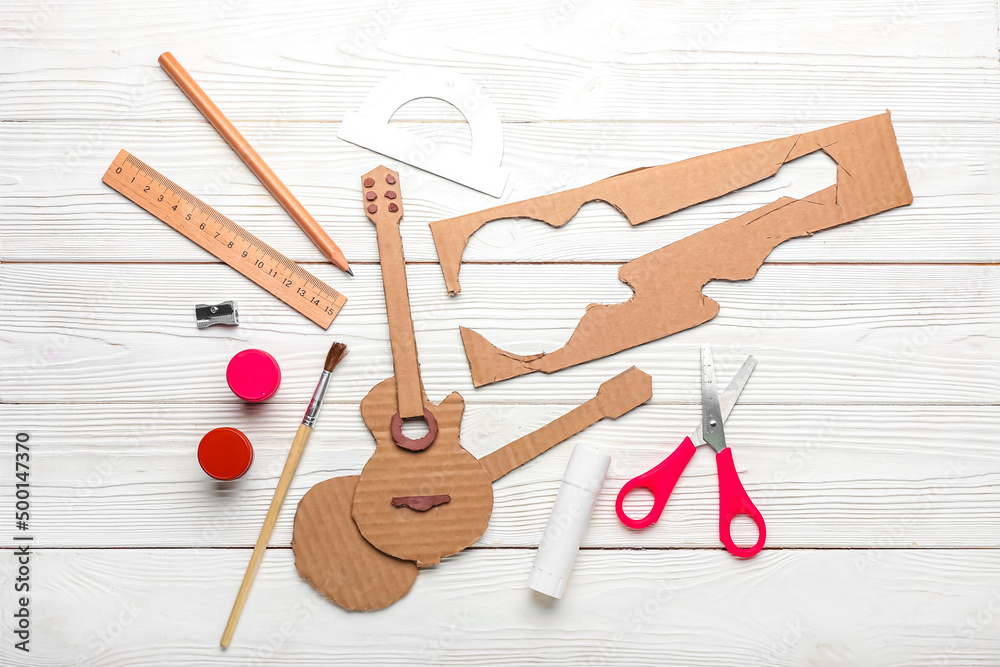 Cardboard guitar toy with materials on white wooden background