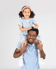 Poster - Portrait of little African-American girl sitting on shoulders of her father on grey background