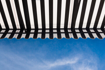 Poster - black and white striped awning against blue sky background.